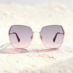 Beach sand texture background photo of AvilaDubee DB7258 rose gold square sunglasses, lavender gradient tint UV400 lenses ideal for summer vacation and beach travel outfits