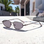 Outdoor patio lifestyle photo of AvilaDubee vintage slim oval copper alloy sunglasses, rose gold frame light purple anti-UV nylon lenses minimalist retro eyewear for summer vacation street photoshoots