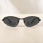 Front view minimalist white background photo of AvilaDubee slim angular Y2K sunglasses, matte black thin metal frame dark grey anti-UV lenses modern city travel street style eyewear